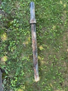 Piece of rusted copper piping with holes in it laid in the grass outside of a Virginia home
